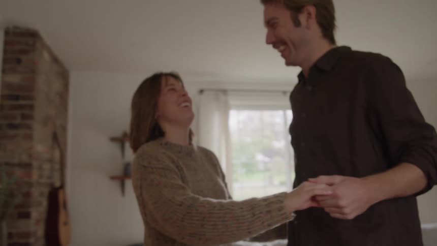 Young man and woman dancing and laughing in a living room indoors during day time