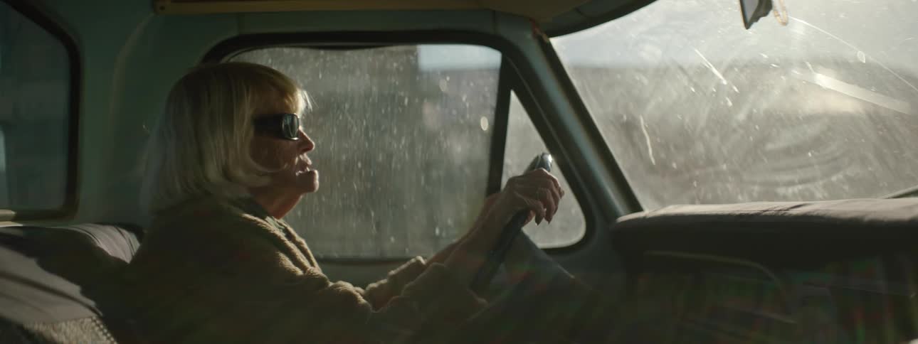 A blind old woman is sitting in the driver's seat of a pickup truck
