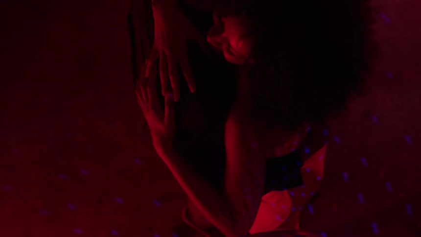 A man and a woman dances while embracing each other in a lowlight environment illuminated by red and blue party lights