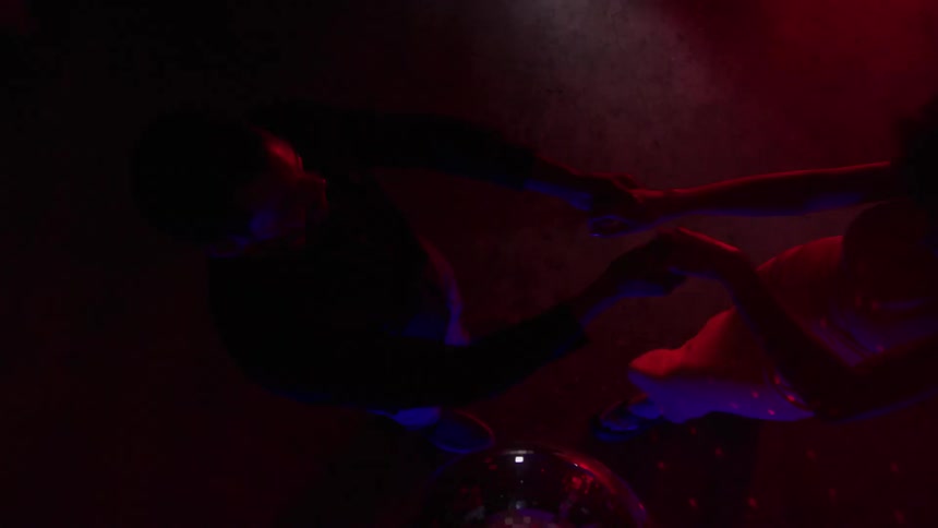 Couple dances under red light reflected by a disco ball