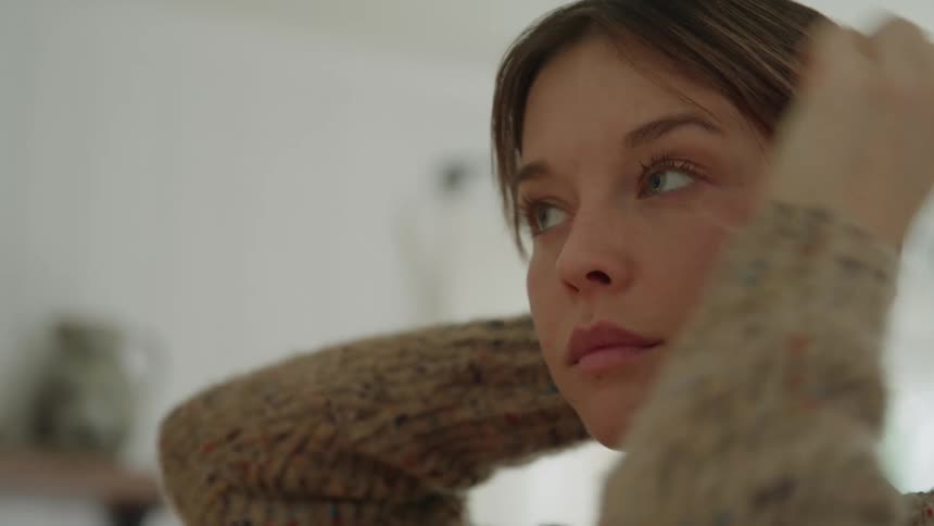 A womans face as she uses her hands to touch her hair and ear wearing a textured knit sweater then she looks up and her head is approached by a man who kisses her in the mouth