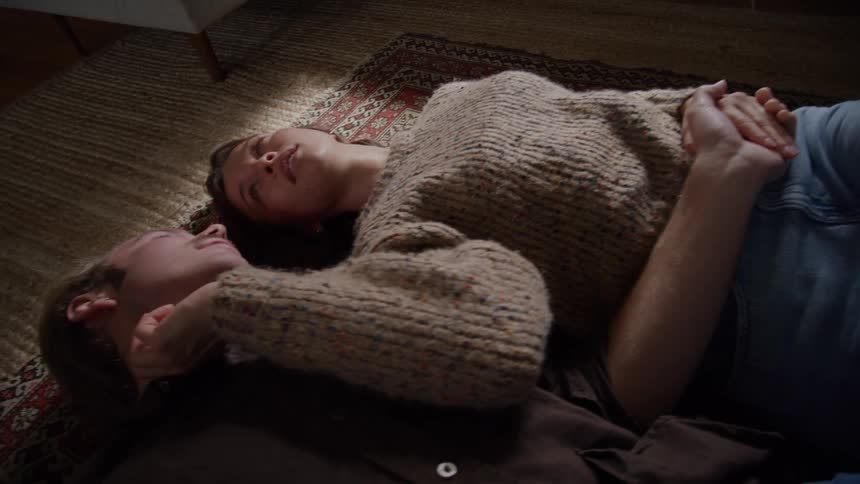 Couple lies side by side on the rug sharing a calm gaze
