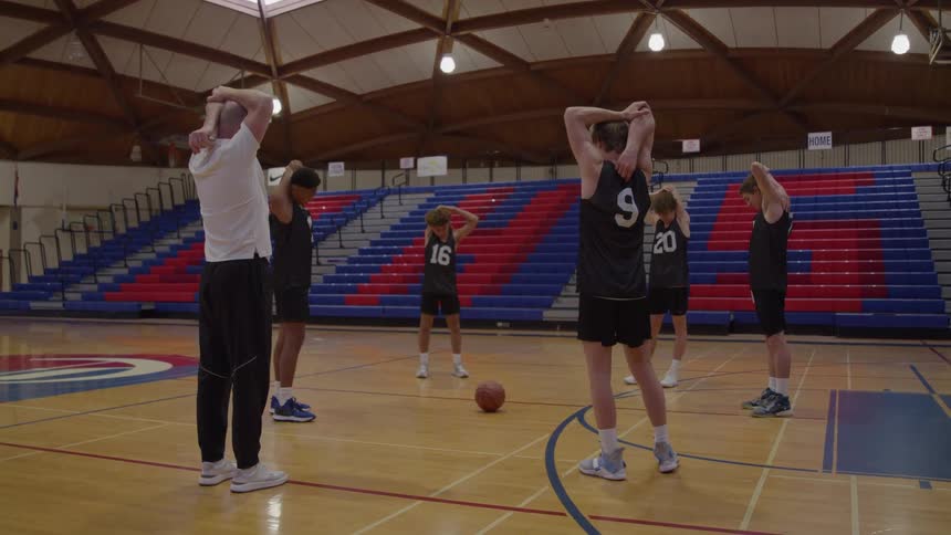Coach and players stretch their arms during basketball practice