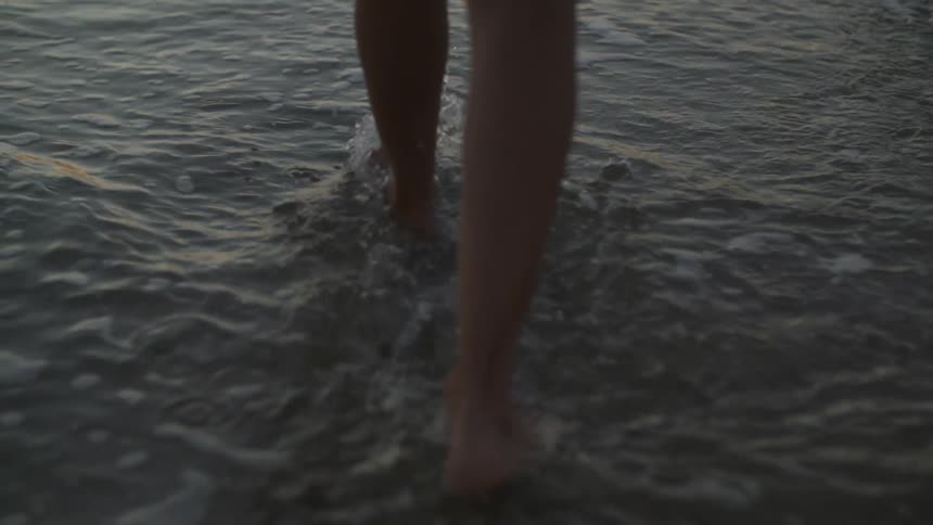 A woman walking barefoot through the edge of water as it washes on shore