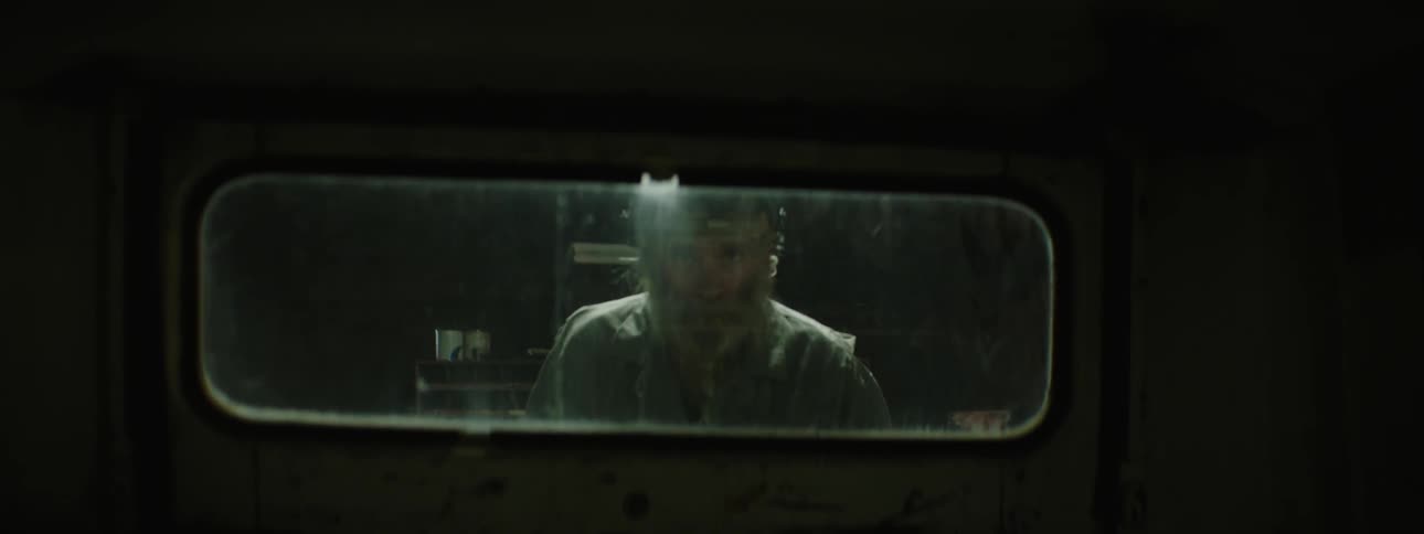 A man in a welding helmet looks out the window at flashing lights
