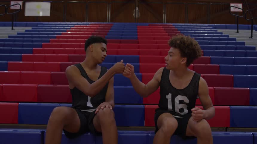 Two male teenage athletes perform a special handshake in a sports arena