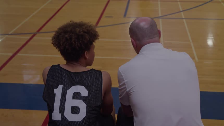 Close up of a coach conversing with a teen athlete in a basketball court