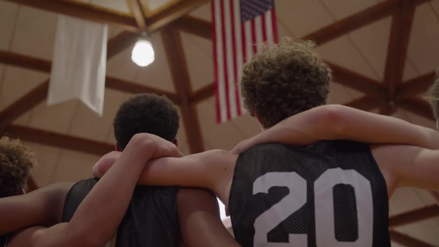 The team stand with their arms over each others shoulders underneath a flag