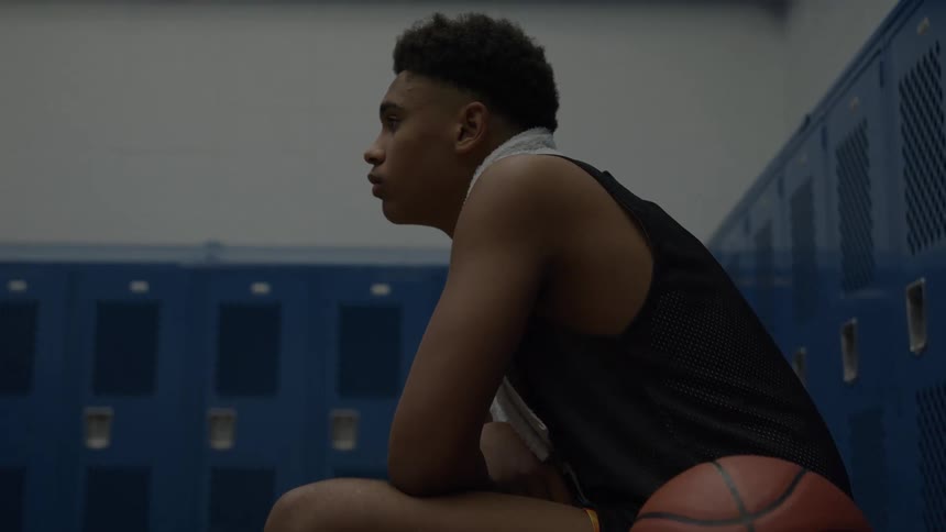 A black male basketball athlete sitting in a locker room after a game