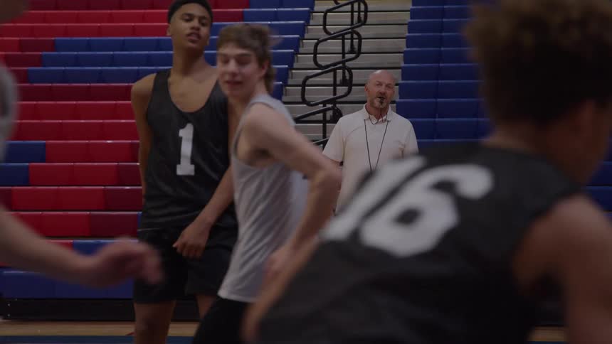 Coach watches closely as players practice basketball