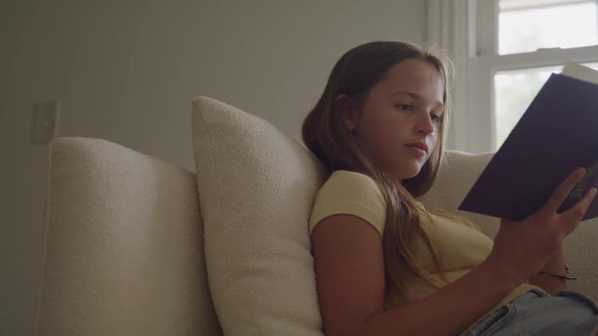 Young girl reads a book while sitting on a couch in a living room