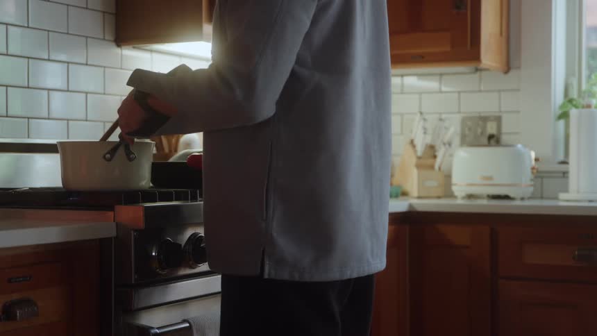 Person stirs a pot on a stove with a wooden spoon in a kitchen