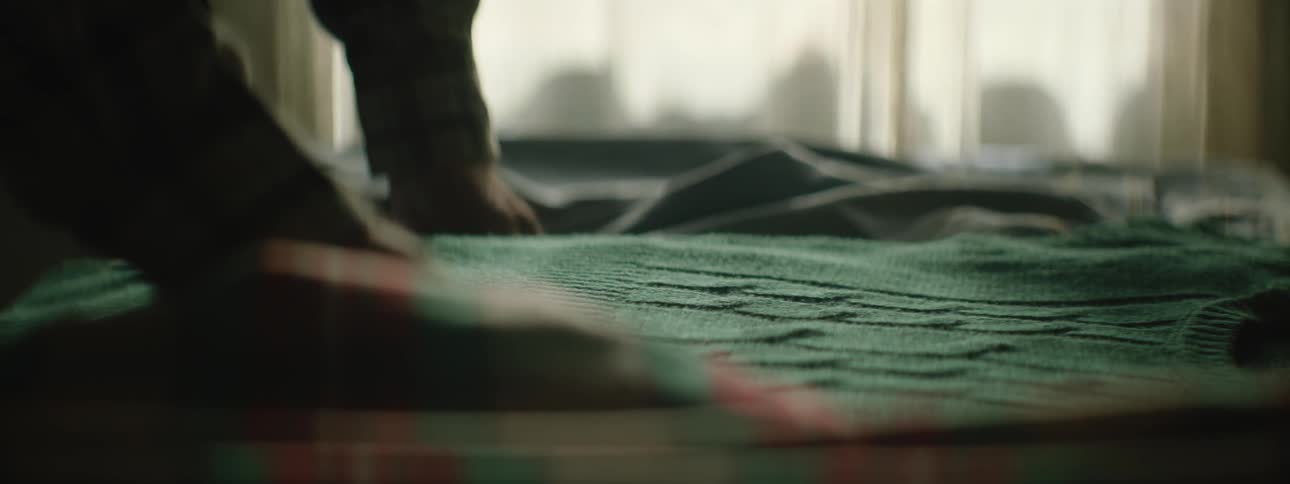 A person smooths down a sweater that is lying on a bed
