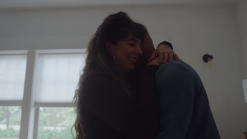 A couple embraces admiring a pregnant belly in a bright bedroom
