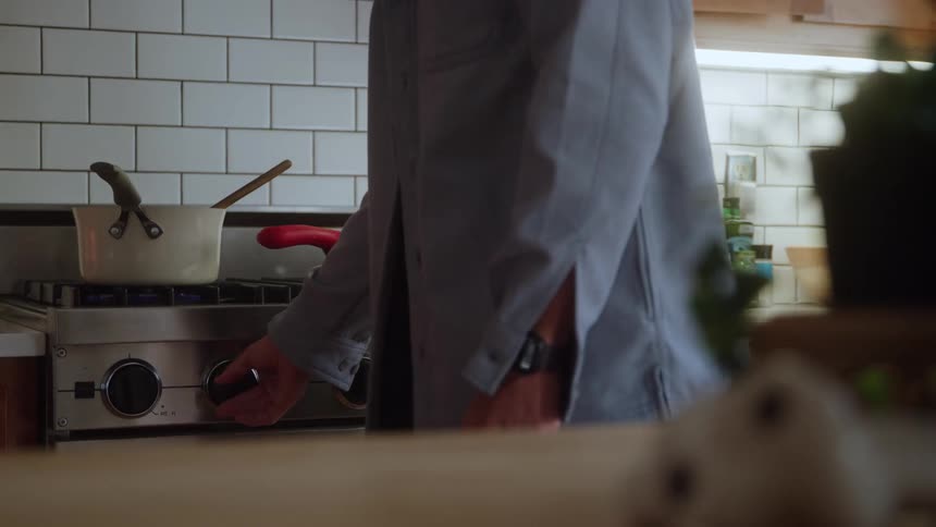 Man turns on the stove and stirs a pot sitting on a burner
