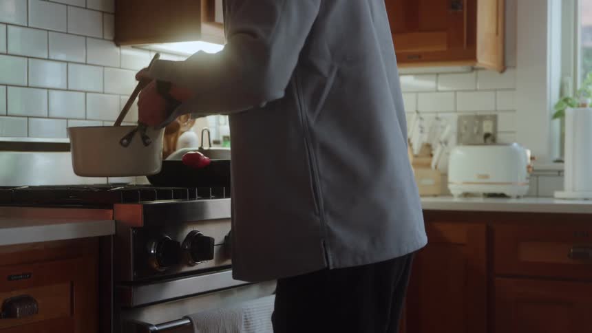 A person stirs food in a white pot on the stove in a modern kitchen