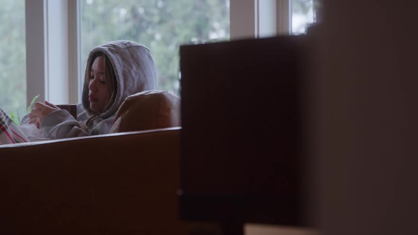 A female in a hoodie holding a mug wipes her nose appearing sick