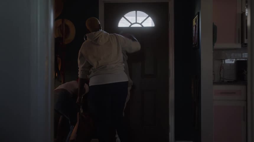 A view from inside a dark hallway shows mother rushing her children as they go out the front door closing it quickly behind them