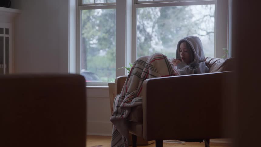 Person sits comfortably on a couch sipping coffee at home