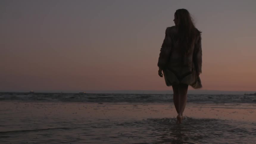 Woman walking into water at sunset