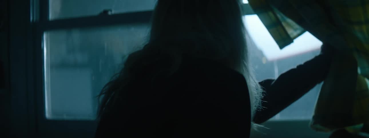 An older woman looks out a window toward a flashing light