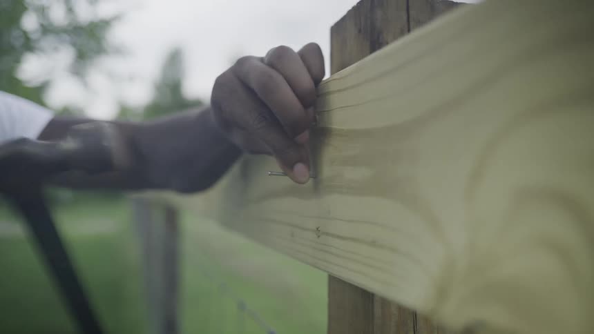 A man hammering in a nail on a piece of pine wood outdoors