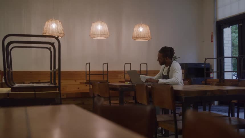 Small business owner working on a laptop at a wooden table in his cafe