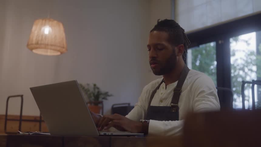 A young male business owner working with laptop in his cafe
