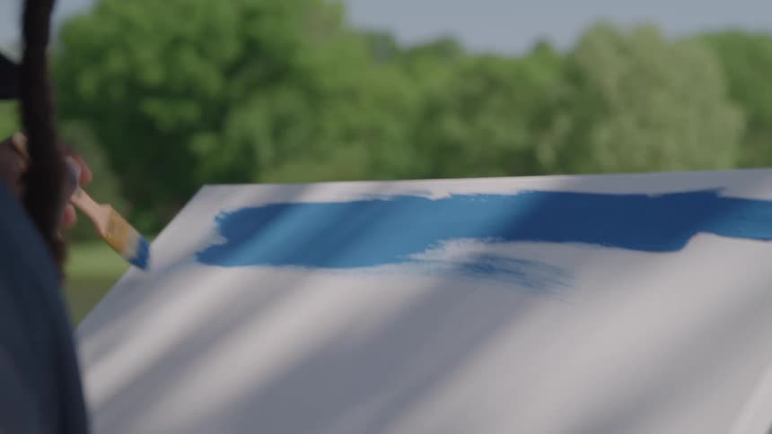 An artists hand painting a bold blue stroke across a white canvas
