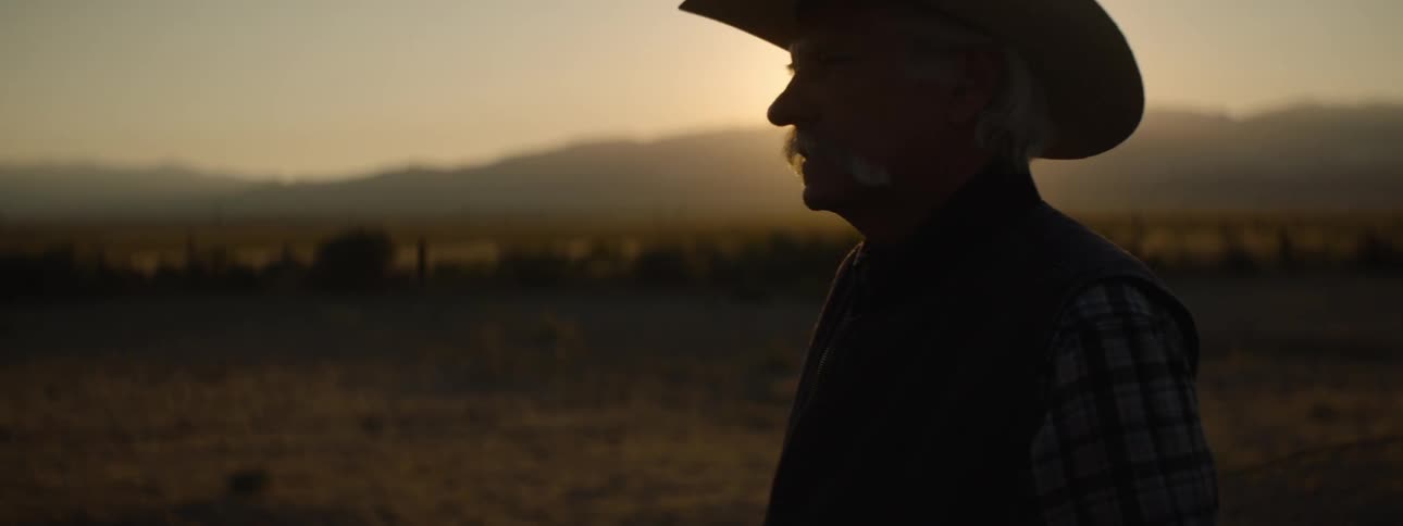 An old cowboy stands in a rural area