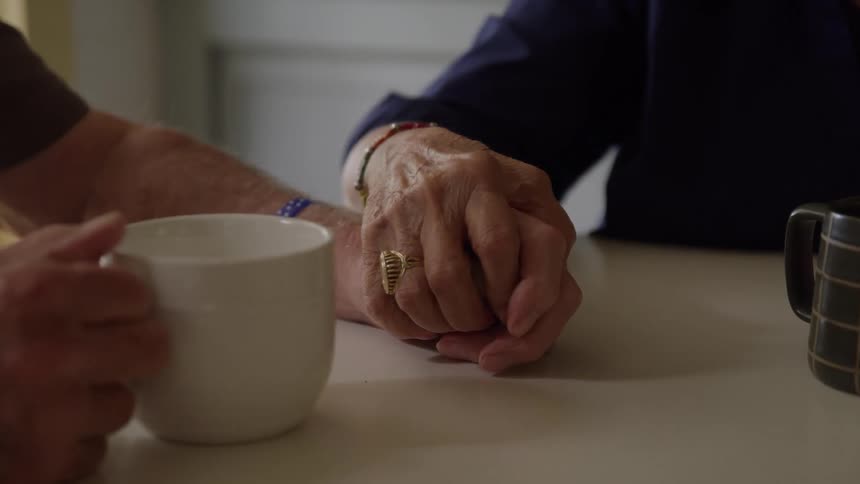 Closeup of an elderly couple holding hands at a cafe table