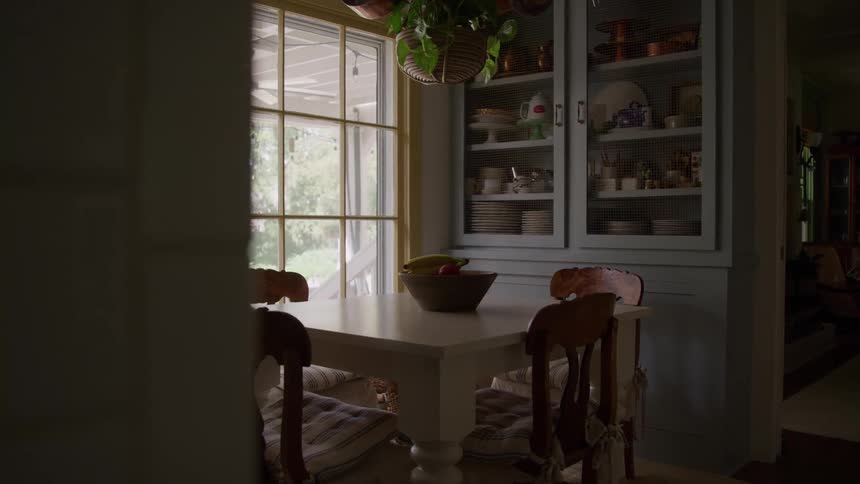 A sunlit rustic dining nook with a large window looking out onto a porch