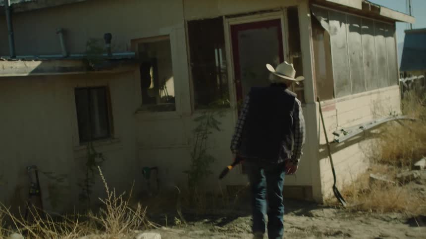 A man in a cowboy hat carries a gun into a rural house