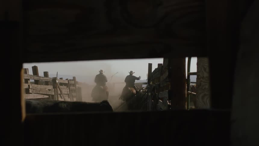 Two cowboys ride horses near wood fences and cattle