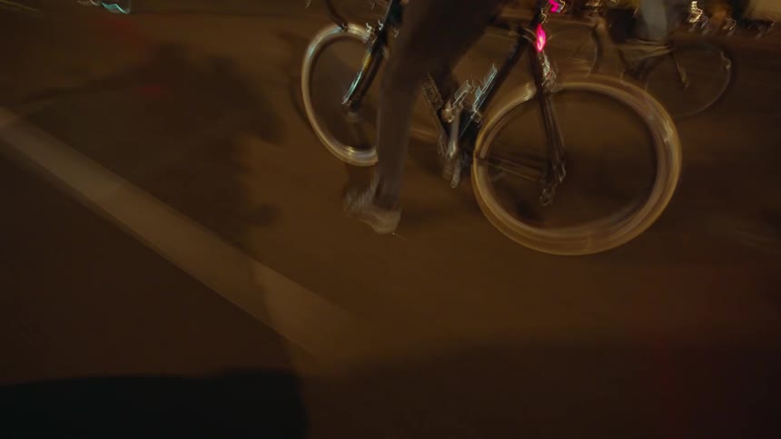 Cyclists speed through a lit avenue at night