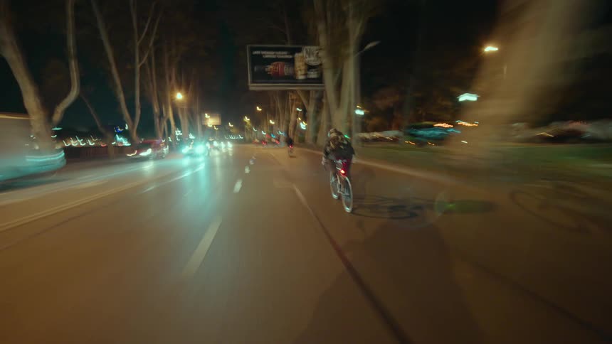 Cyclists ride on a lit street at night