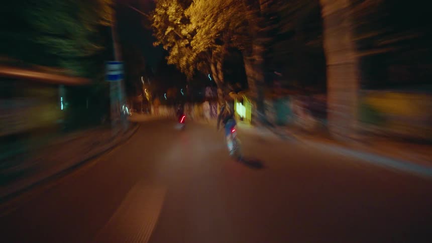 Two cyclists ride along a lit street at night
