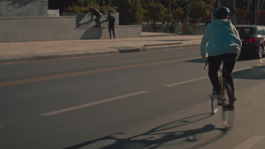 Cyclist in a blue hoodie rides along a busy avenue under the afternoon sun