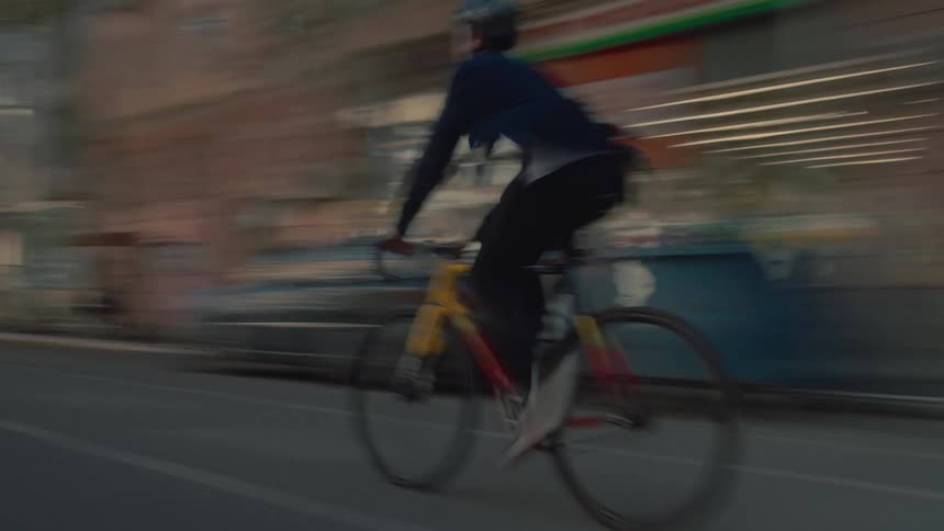 Cyclist wearing a helmet rides along an urban street at sunset