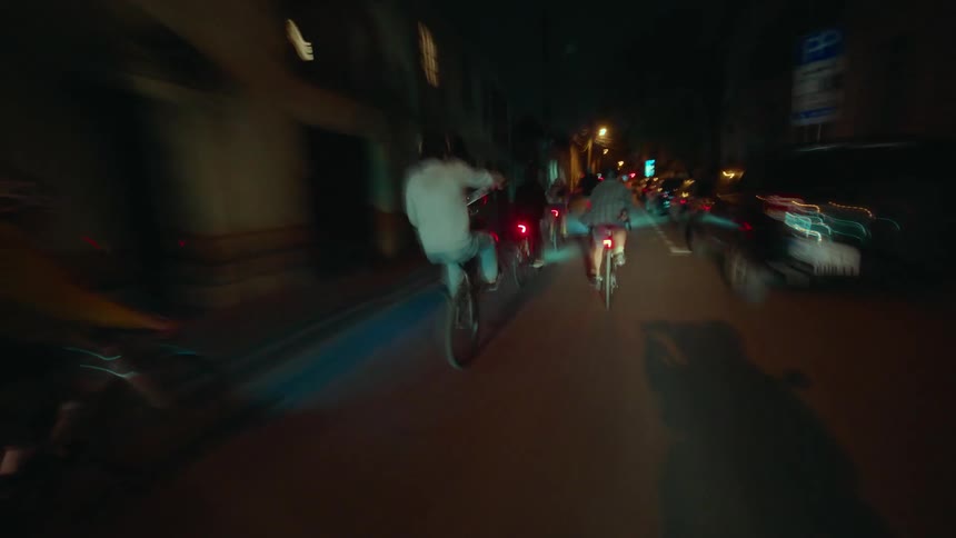 Group of cyclists rides through a lit street at night