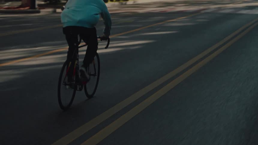 Cyclist in a blue hoodie rides across an empty avenue in the morning