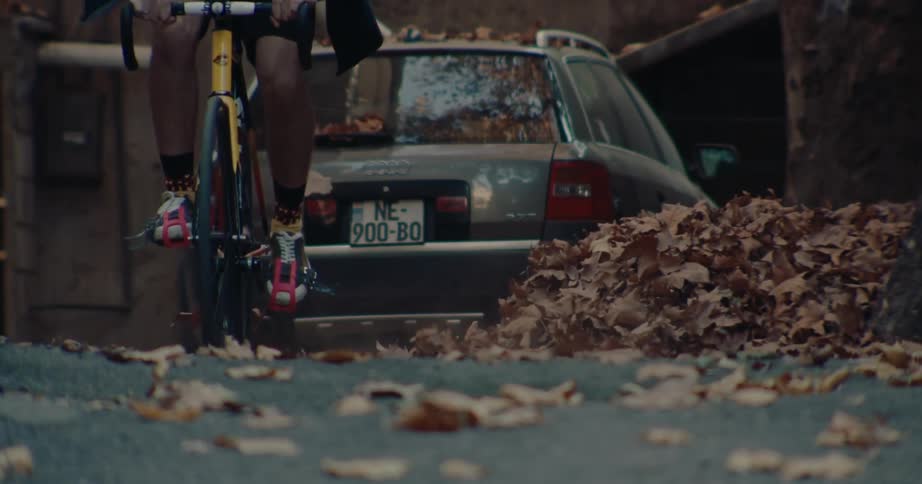 Cyclist rides along a street covered with dry leaves beside a parked car