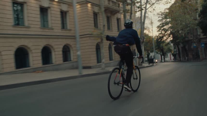 Cyclist rides through a treelined street between buildings at dusk