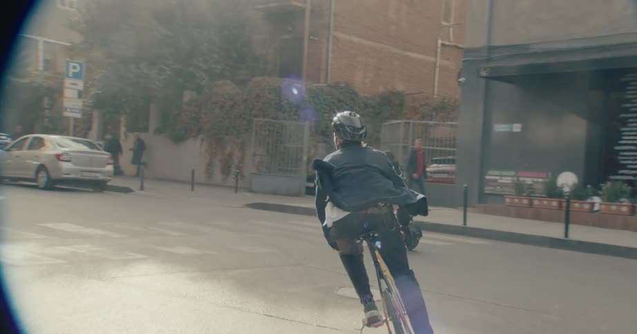 Man wearing a denim jacket cycling through a busy street on a suburban area outdoors during day time