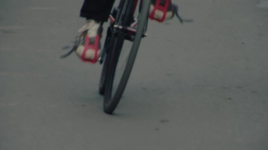 A person is riding a yellowframed bicycle on an asphalt road filmed from a low angle that prominently displays the front wheel and the persons feet rotating the pedals