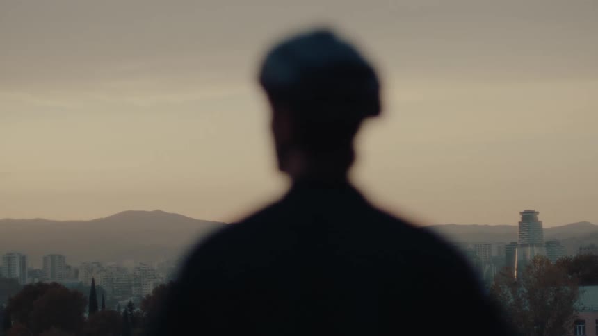 Silhouette of a person watches the city at sunset with mountains in the background