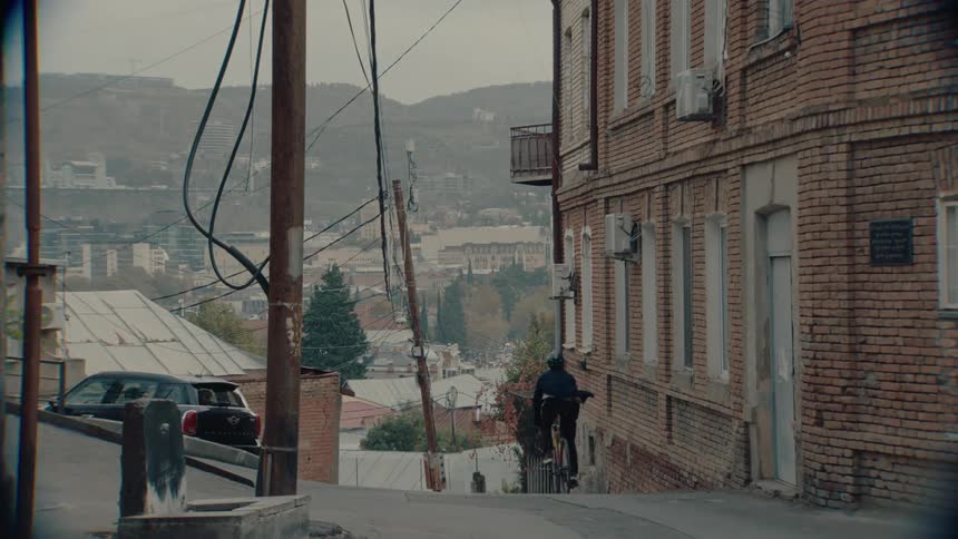 Cyclist rides down a narrow street lined with brick buildings overlooking the city