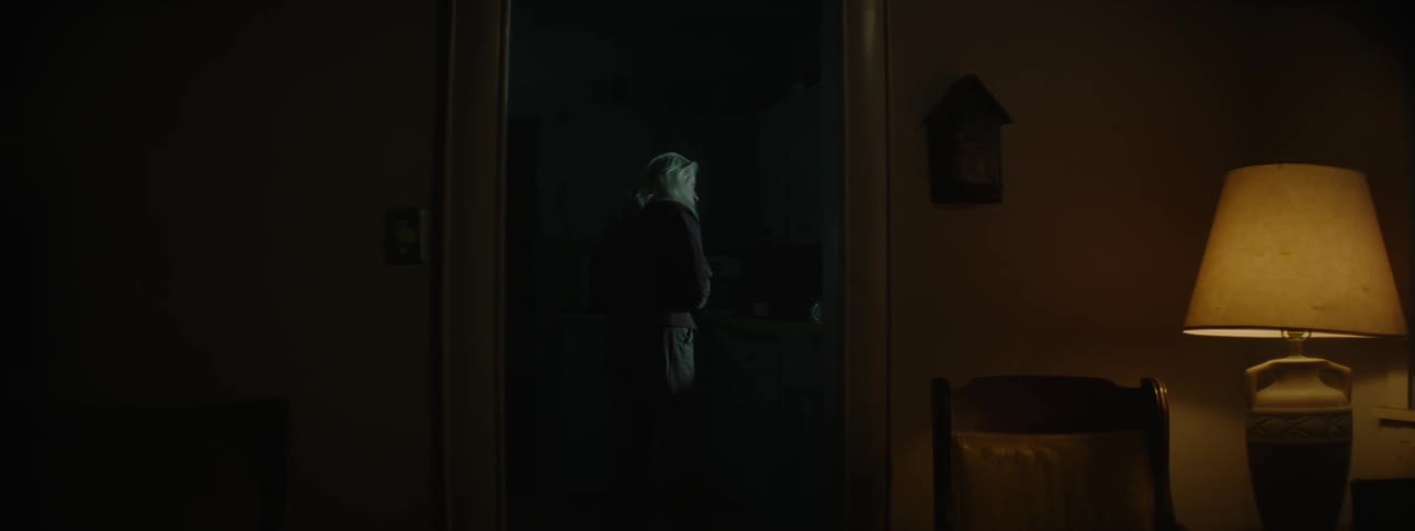 A woman watches outdoor lights through a kitchen window