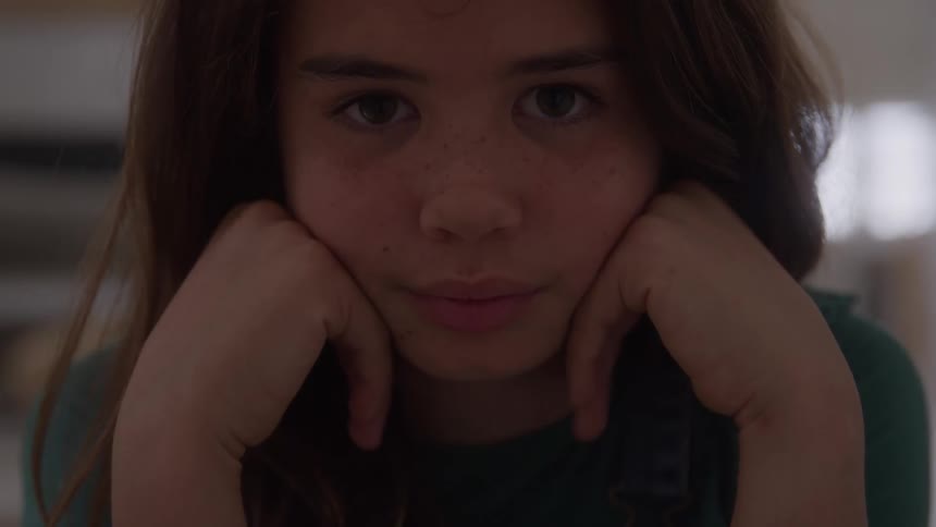 Girl rests her face on her hands looking straight ahead with a calm expression