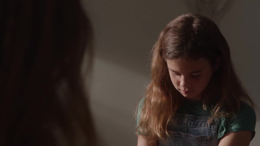 Girl in denim overalls looks down with a thoughtful expression in sunlight